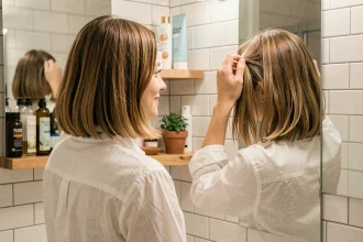 Jeune femme adoptant un style de coiffure tendance et abordable devant son miroir de salle de bain avec des produits capillaires économiques
